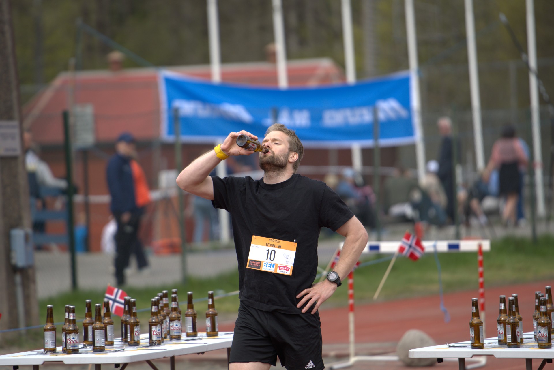 Løper med startnummer 10 tømmer en øl, flasker og flagg i bakgrunnen