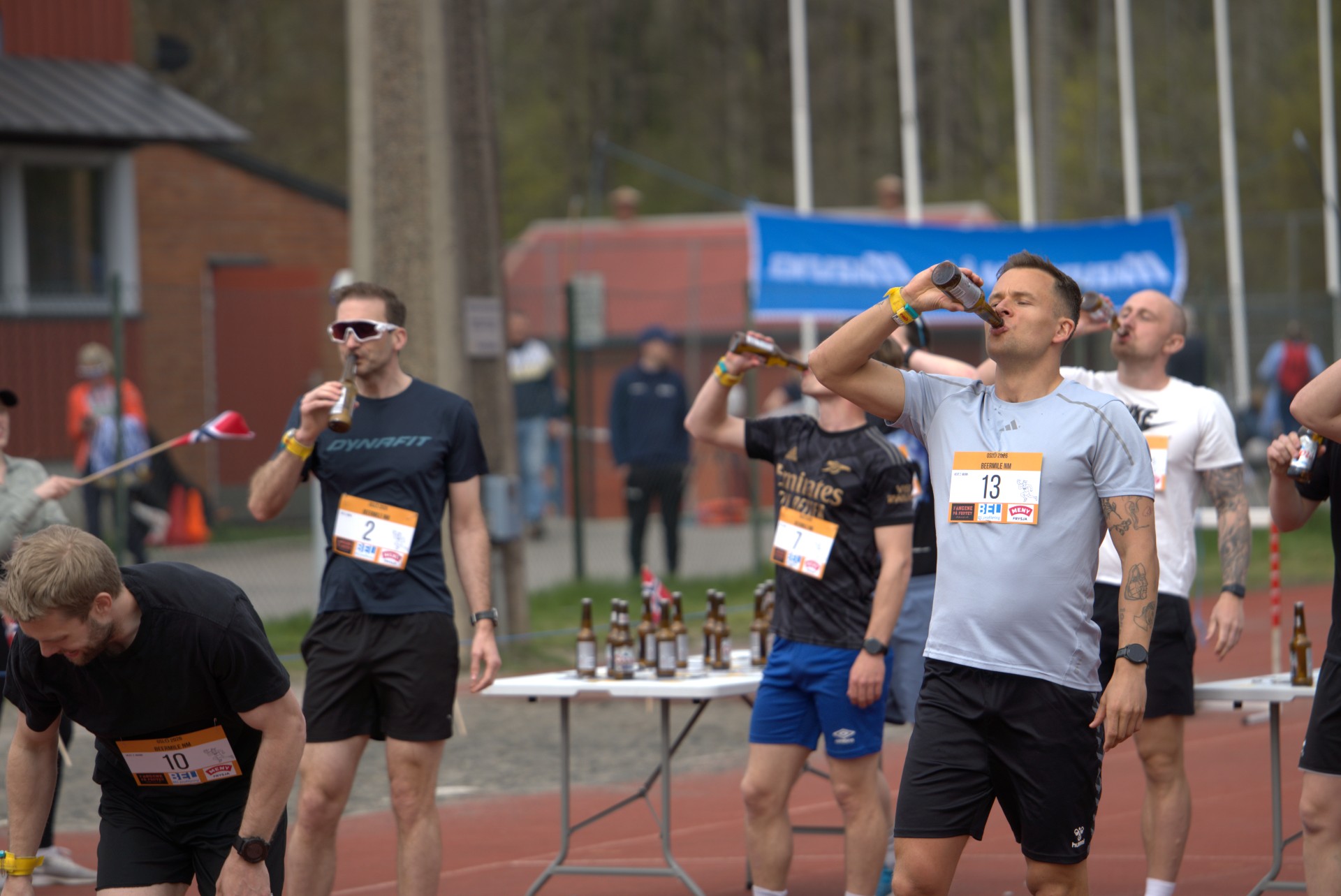 Nærbilde av løper med startnummer 13 som drikker intenst, flasker og flagg synlige