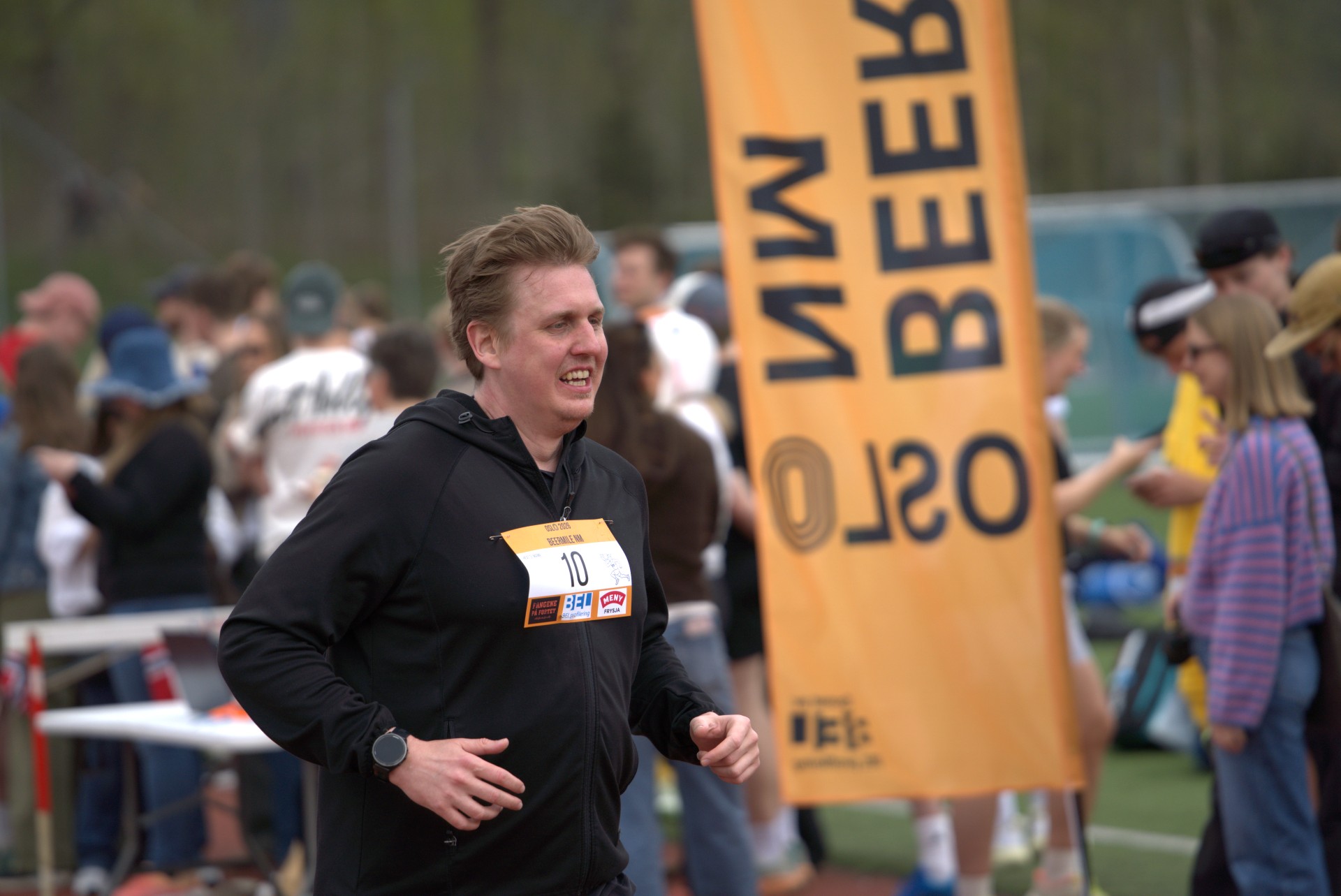 Løper smiler bredt mens han løper forbi BEERMILE NM-banneret